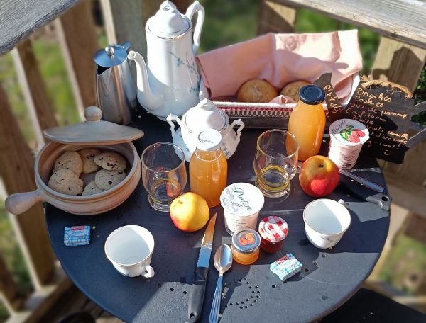 Table en terrasse dun gîte, avec petit-déjeuner copieux et vue sur la nature.