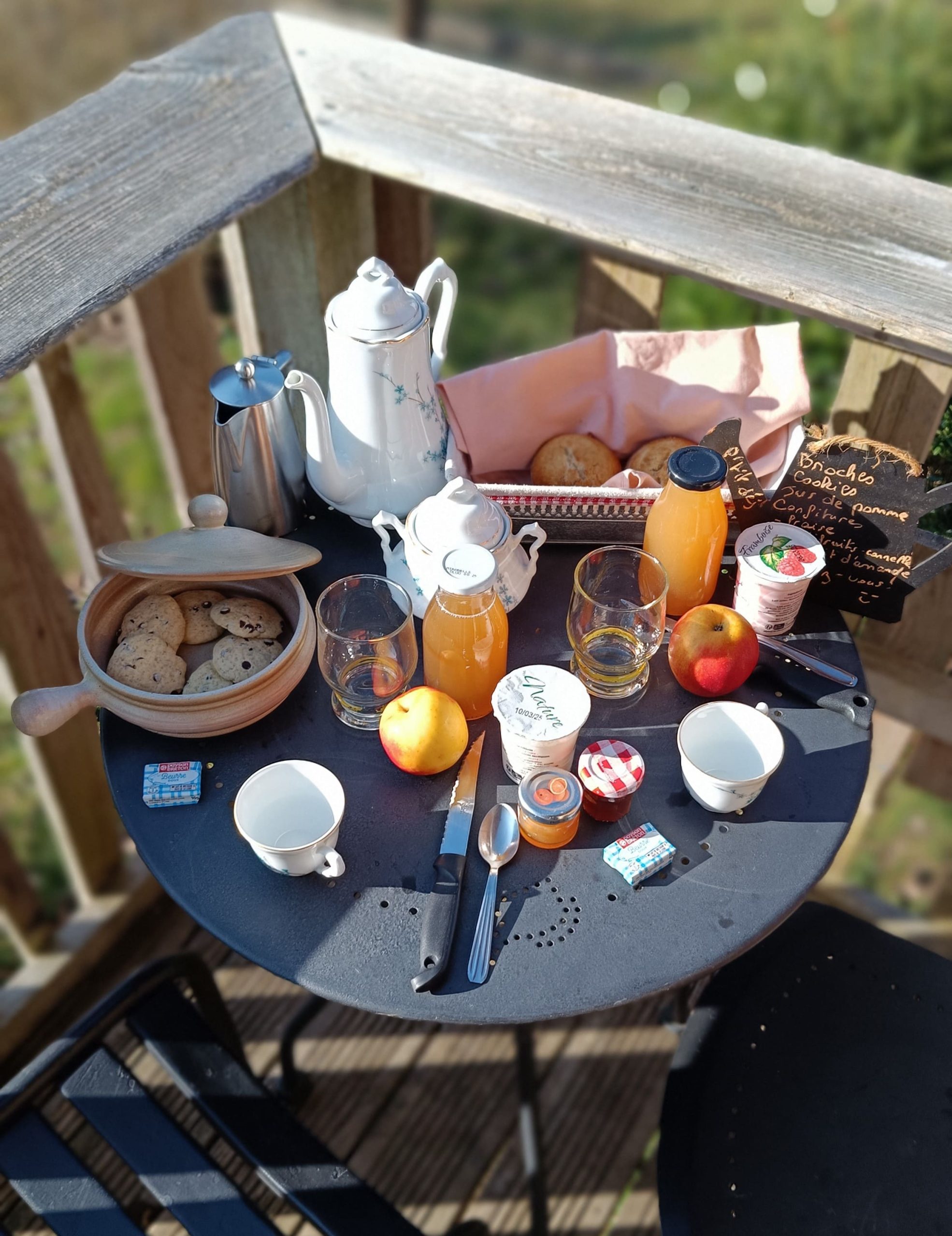 1741355311600 Petit-déjeuner copieux sur une terrasse en bois, avec des fruits, des boissons et des biscuits.