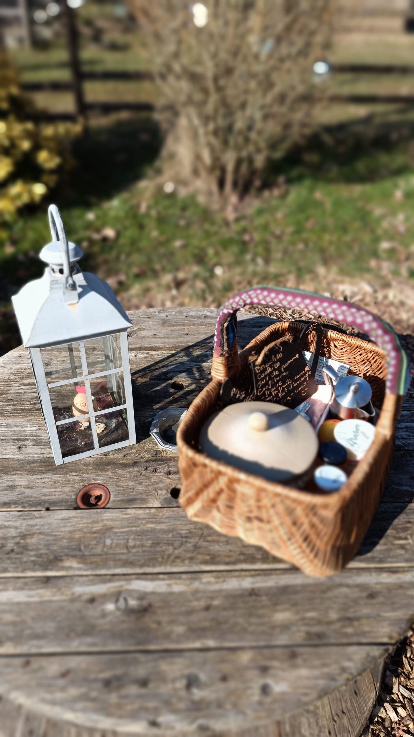 1747308394642 Panier pique-nique en osier sur une table en bois, avec une lanterne et des accessoires colorés.