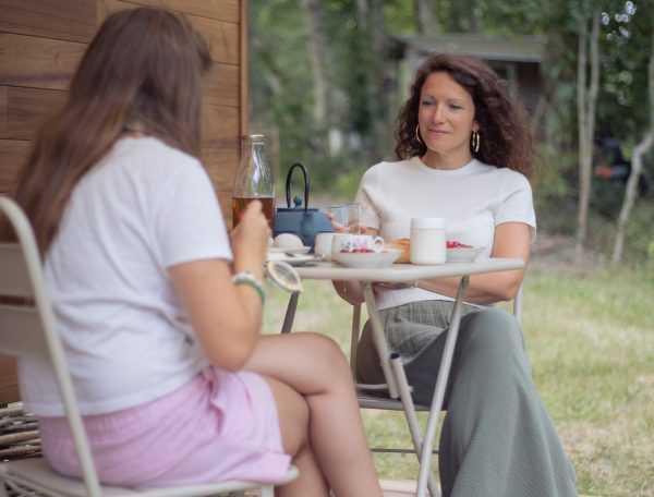 Deux femmes profitent dun petit-déjeuner sur la terrasse dun chalet en bois.