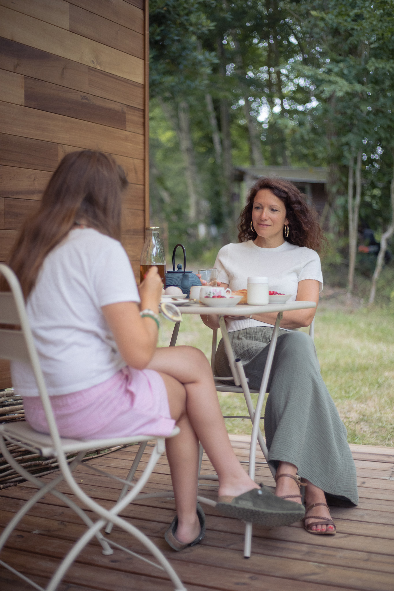 Deux femmes profitent dun petit-déjeuner sur la terrasse dun chalet en bois.
