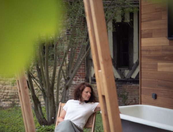 Chalet moderne avec baignoire extérieure, femme détendue sur une terrasse en bois.