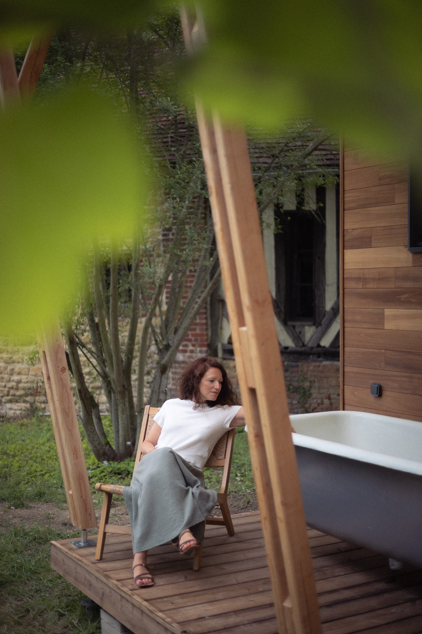 Chalet moderne avec baignoire extérieure, femme détendue sur une terrasse en bois.
