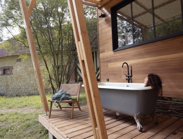Cabane en bois avec baignoire extérieure, entourée de verdure apaisante.