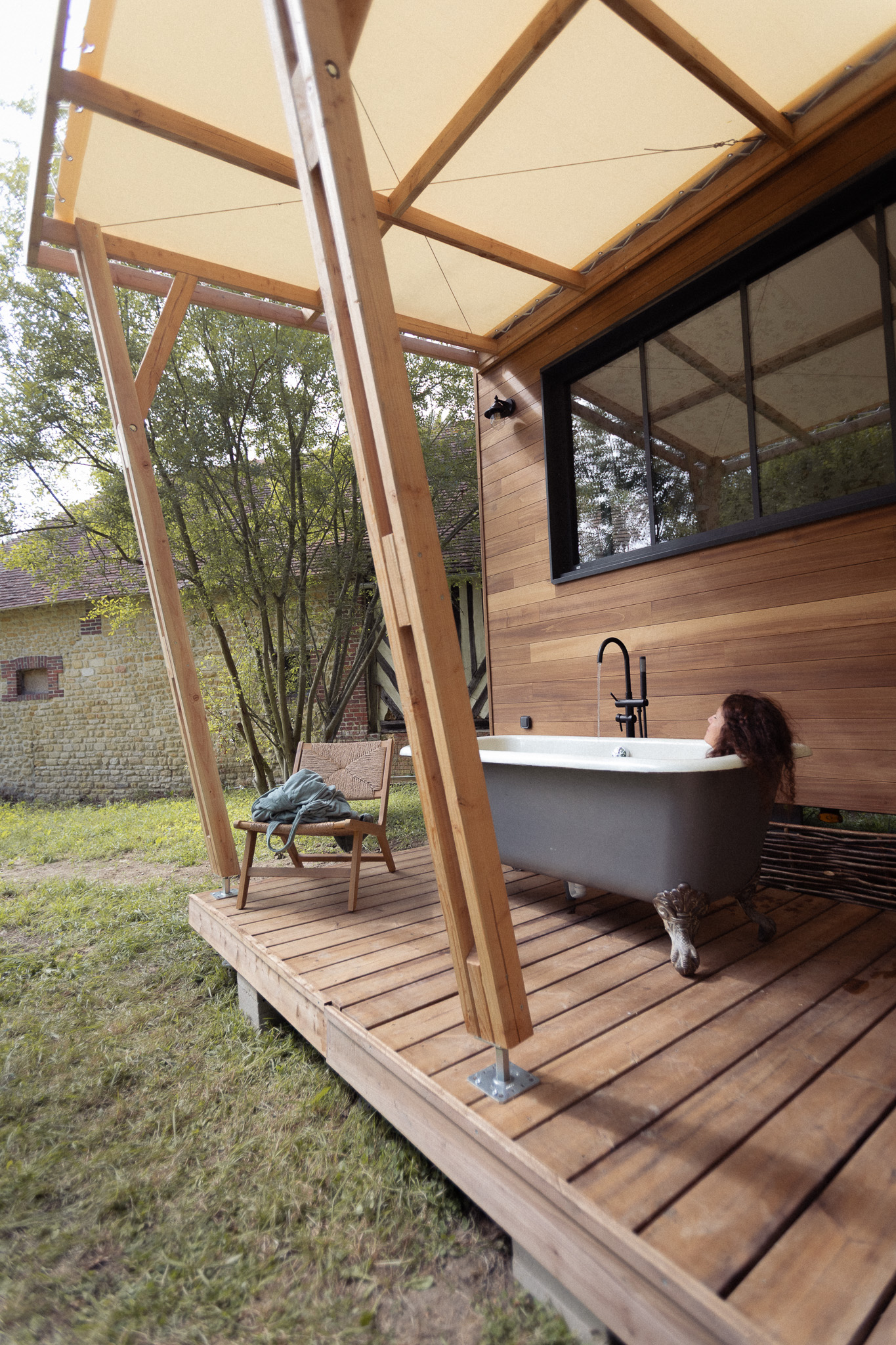 Cabane en bois avec baignoire extérieure, entourée de verdure apaisante.