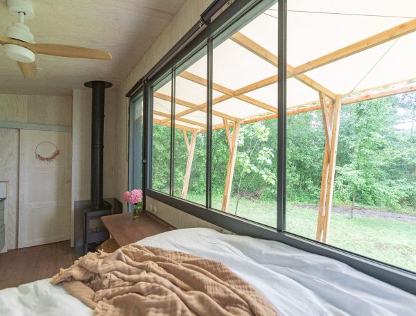 Chalet moderne avec vue sur la nature, lit confortable et grandes fenêtres.