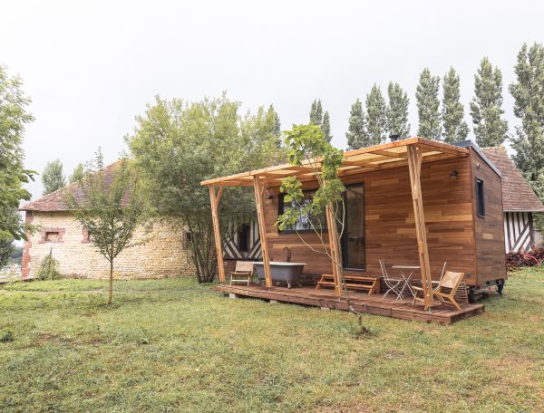 Cabane en bois avec terrasse, entourée darbres verdoyants et dun jardin.