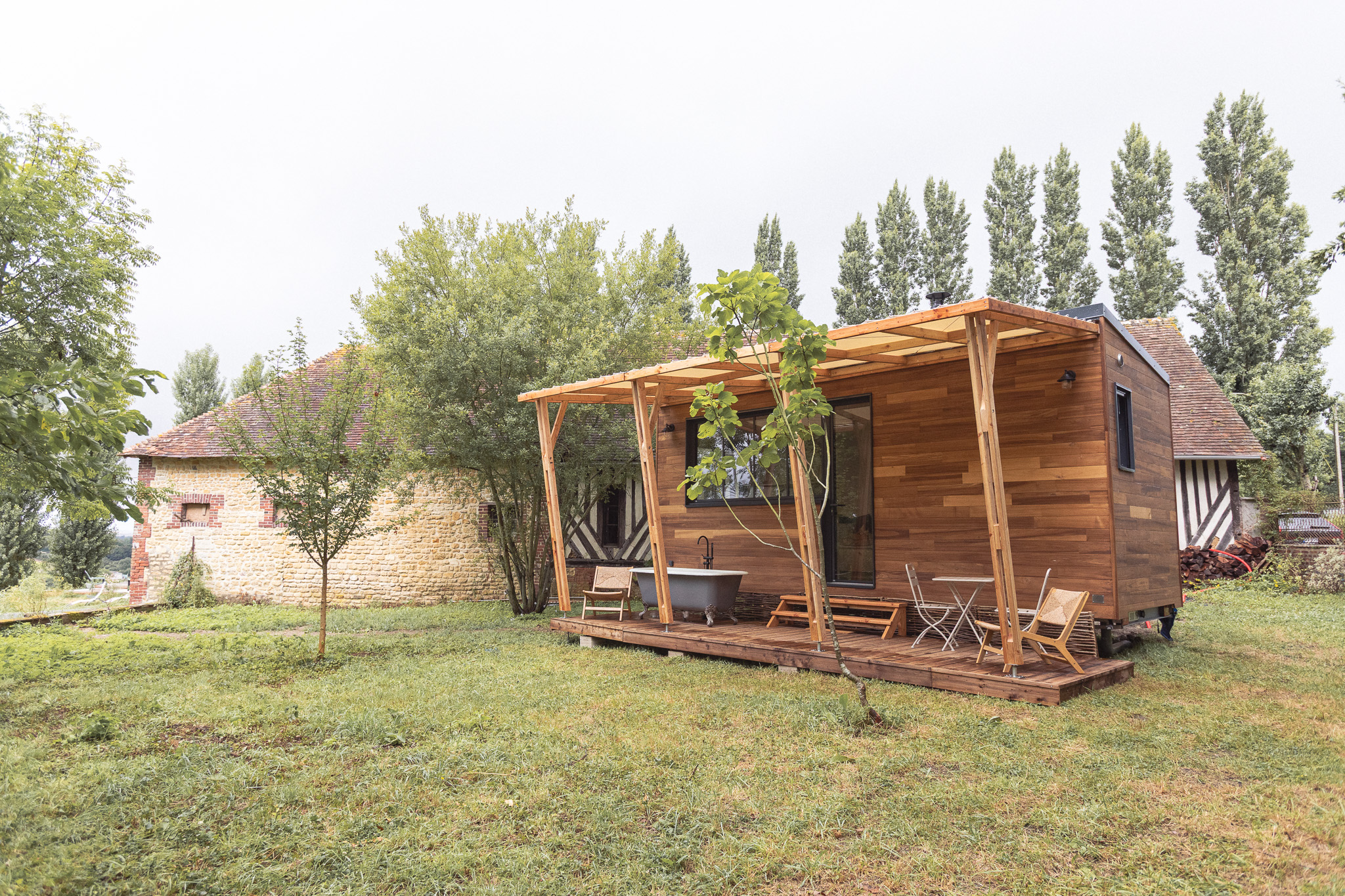 Cabane en bois avec terrasse, entourée darbres verdoyants et dun jardin.