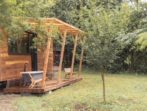 Cabane en bois avec terrasse, baignoire extérieure et verdure environnante.