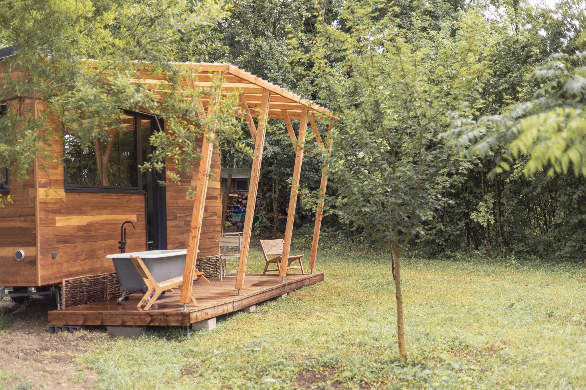 Cabane en bois avec terrasse, baignoire extérieure et verdure environnante.