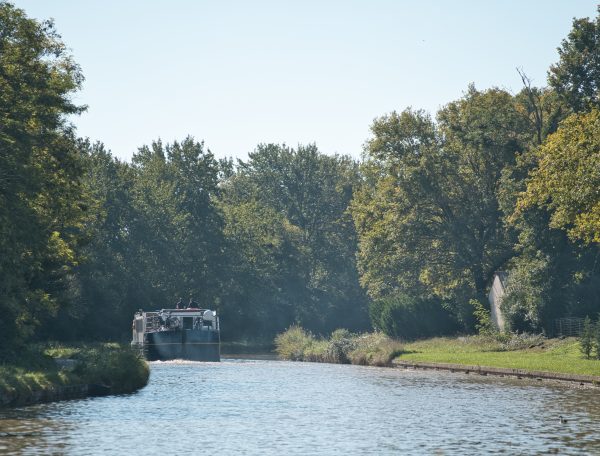 Péniche sur un canal, entourée darbres verdoyants sous un ciel bleu.