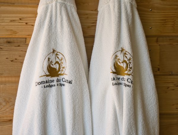 Peignoirs moelleux du Domaine du Canal, lodges et spas, sur un mur en bois chaleureux.