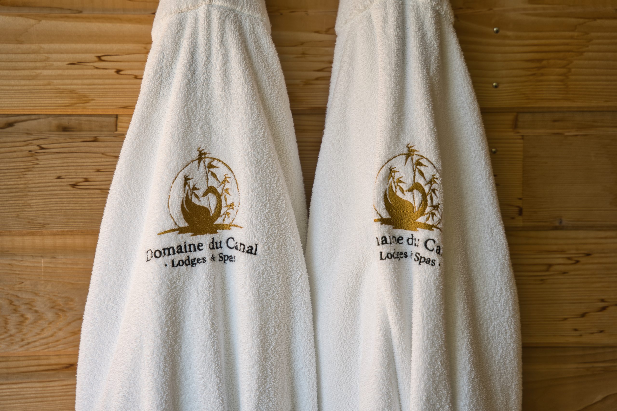Peignoirs moelleux du Domaine du Canal, lodges et spas, sur un mur en bois chaleureux.
