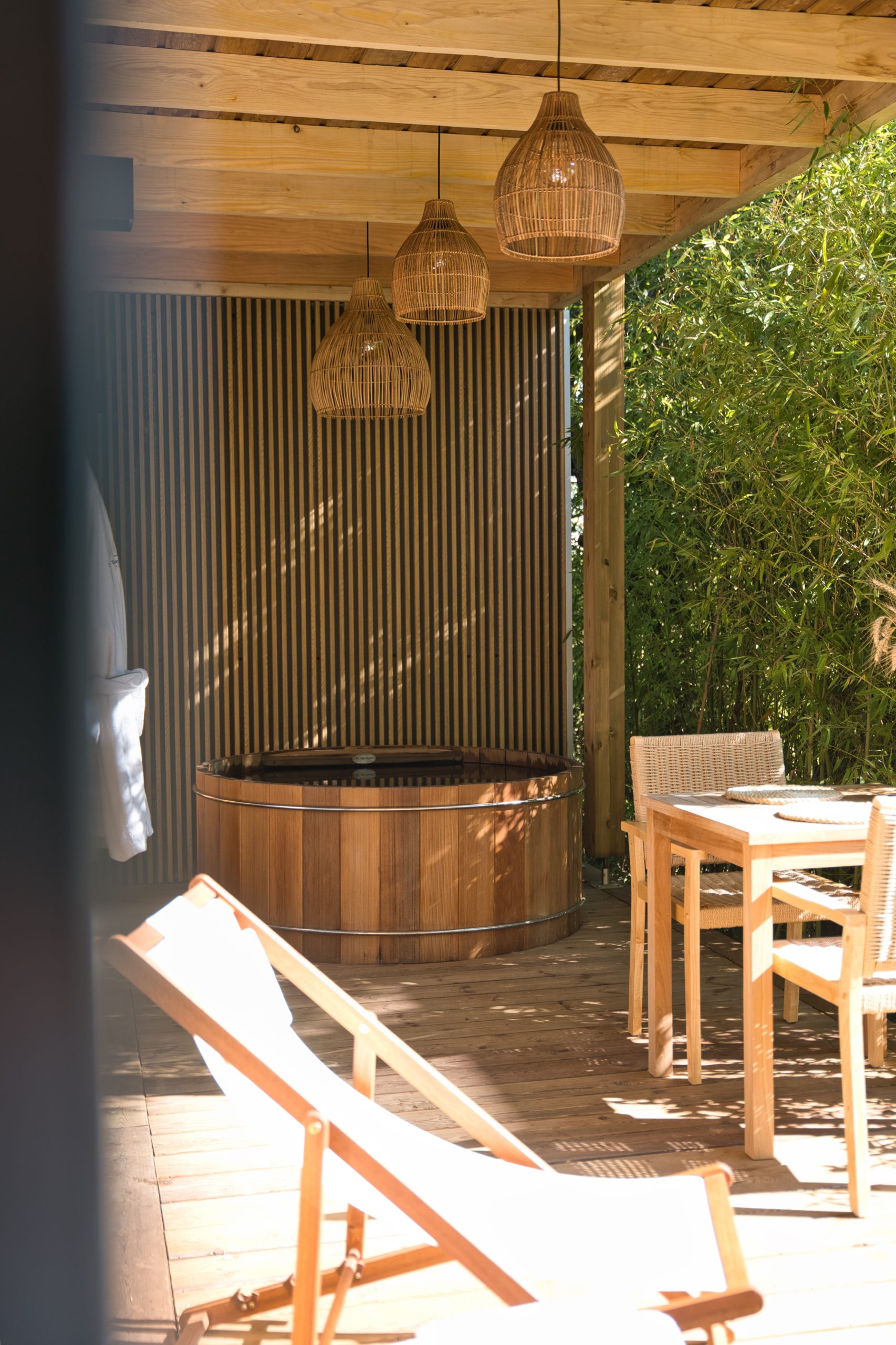 Cabane en bois avec jacuzzi, éclairage suspendu et chaises confortables.