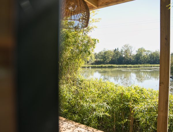 Cabane sur pilotis avec vue sur un étang entouré de verdure luxuriante.