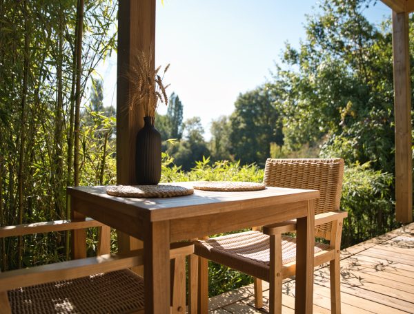 Chalet en bois avec terrasse, table en teck et vue sur la nature verdoyante.