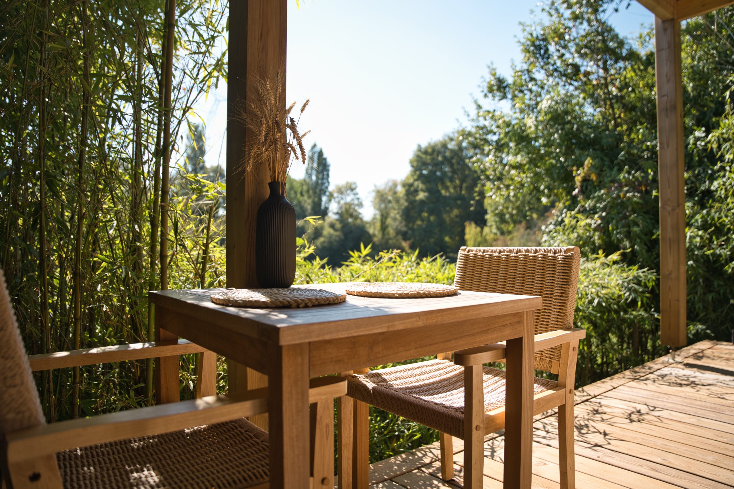 Chalet en bois avec terrasse, table en teck et vue sur la nature verdoyante.