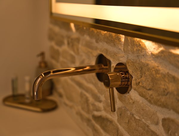 Salle de bain moderne dans un gîte, avec robinet en laiton sur mur en pierre.