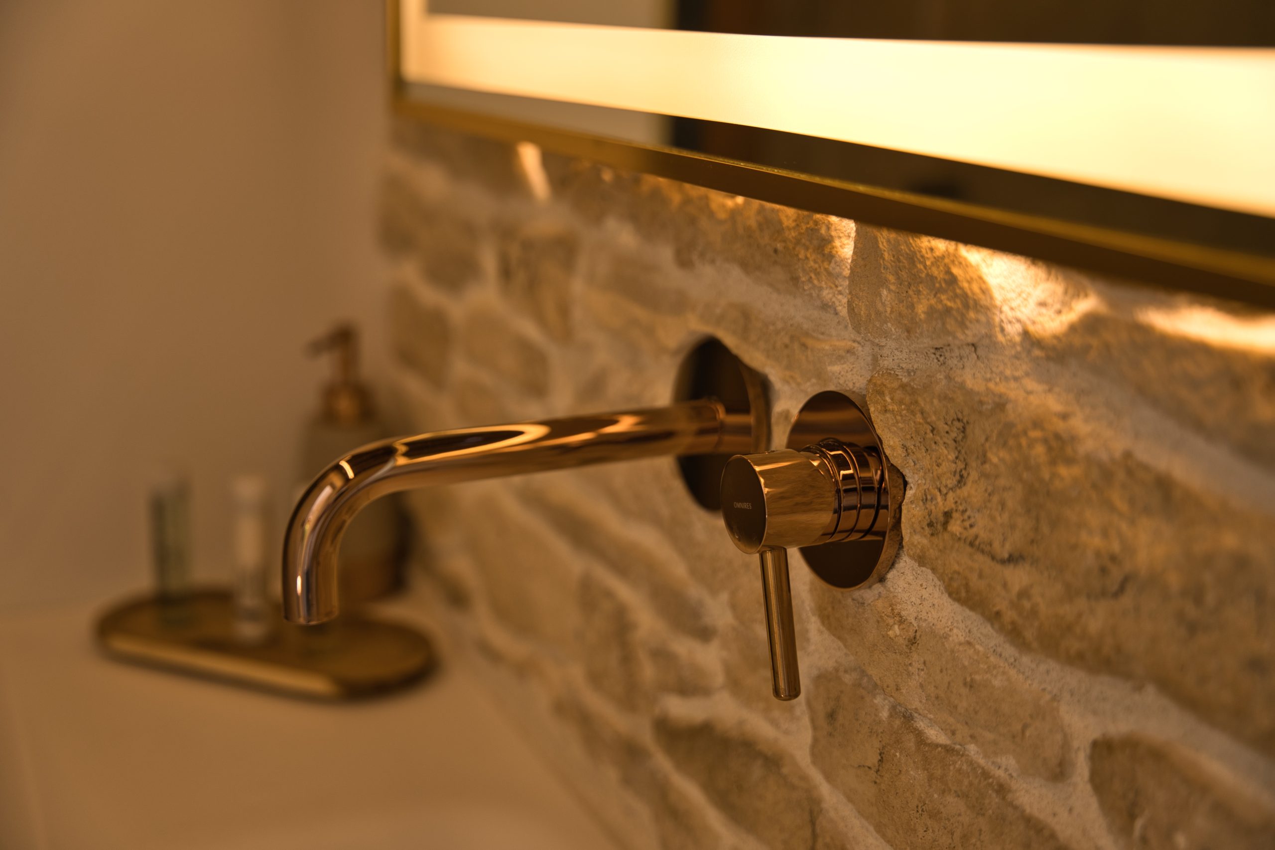 Salle de bain moderne dans un gîte, avec robinet en laiton sur mur en pierre.