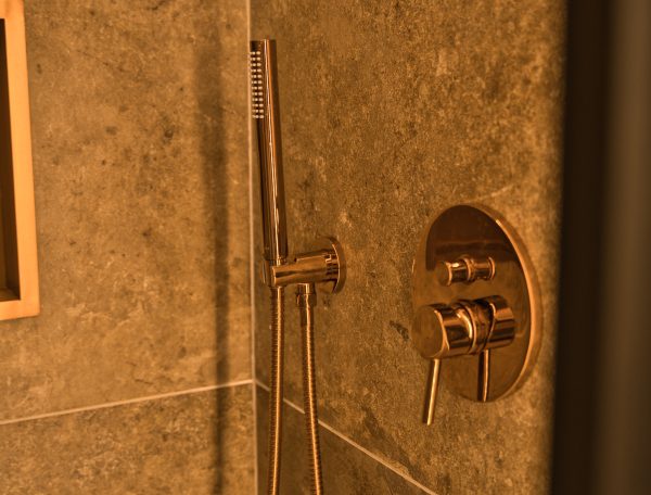 Salle de bain moderne avec douche en marbre et robinetterie dorée élégante.