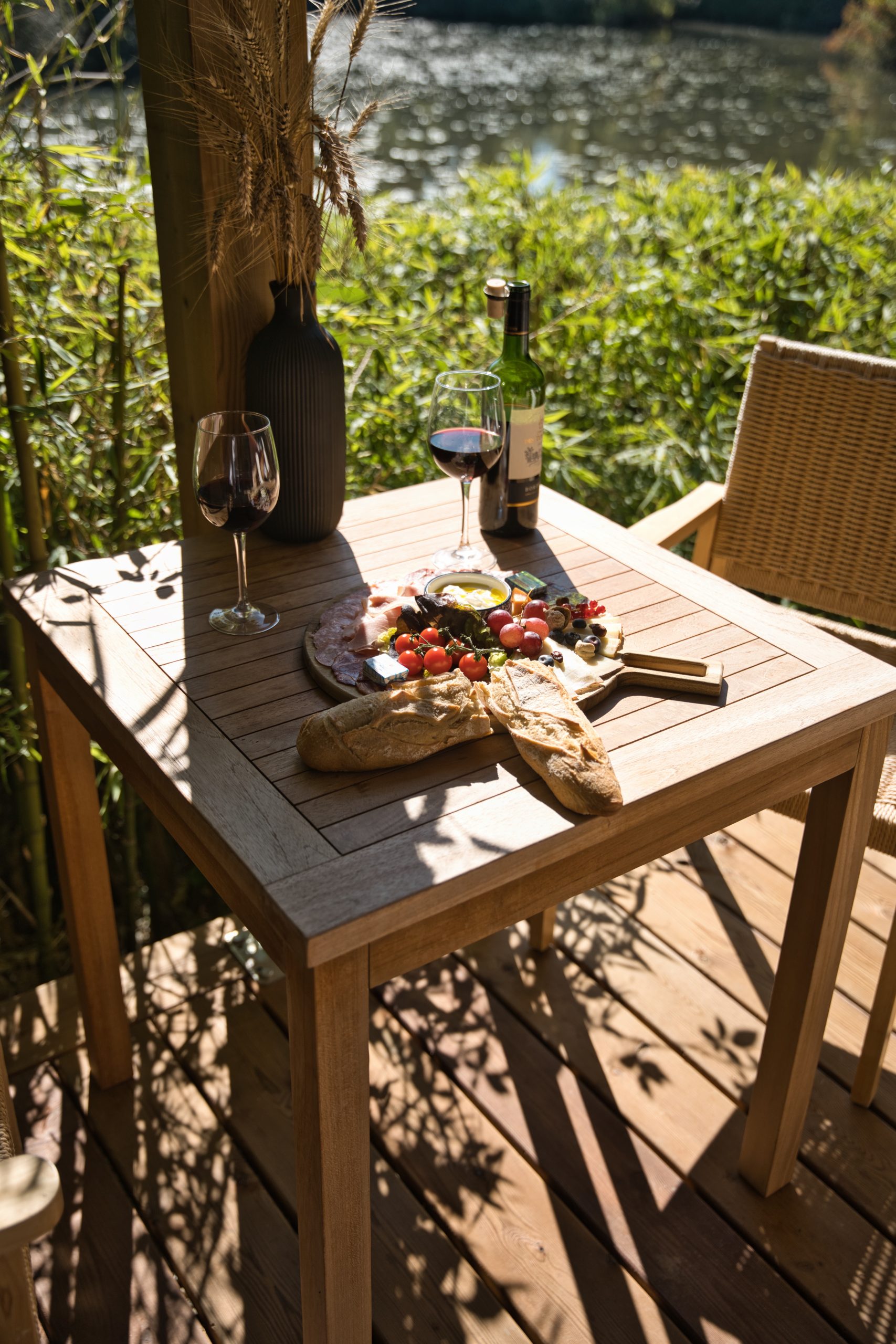 Table en bois avec un repas gourmet et vin, vue sur la rivière. Idéal pour un séjour romantique.