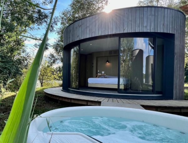 Cabane moderne avec jacuzzi, entourée de verdure et baignée de lumière naturelle.