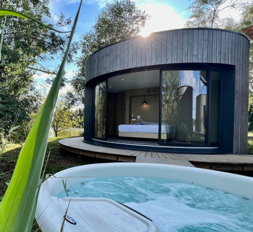 Cabane moderne avec jacuzzi, entourée de verdure et baignée de lumière naturelle.