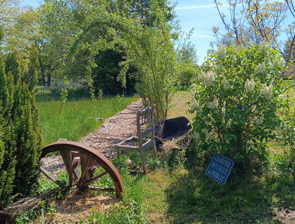 Gîte rural avec un jardin verdoyant et une ancienne roue en bois décorative.