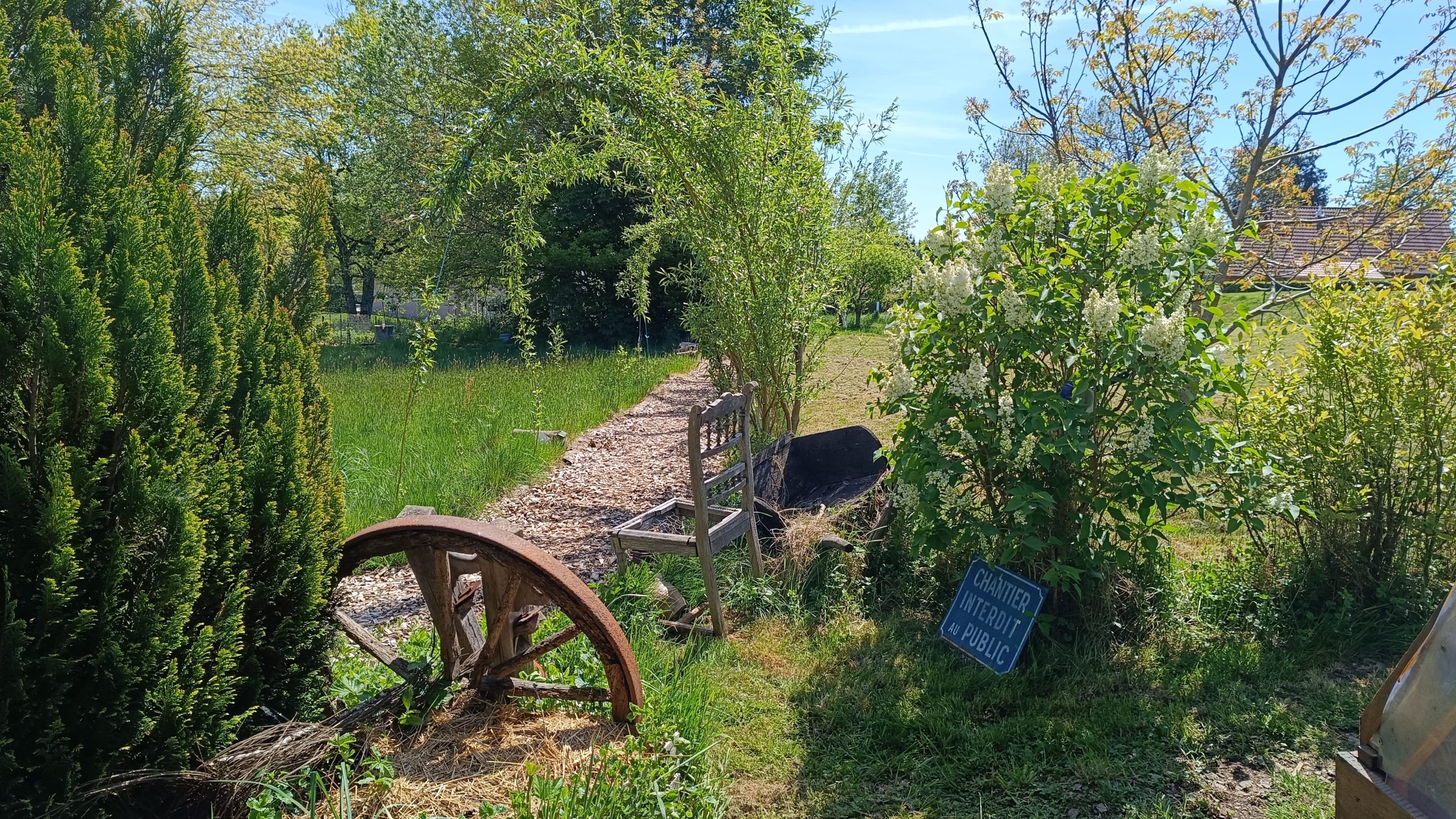 Gîte rural avec un jardin verdoyant et une ancienne roue en bois décorative.