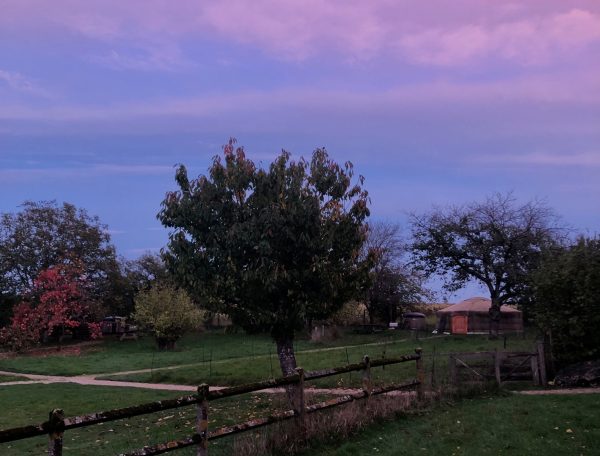 Gîte rural avec un jardin verdoyant et un ciel coloré au crépuscule.
