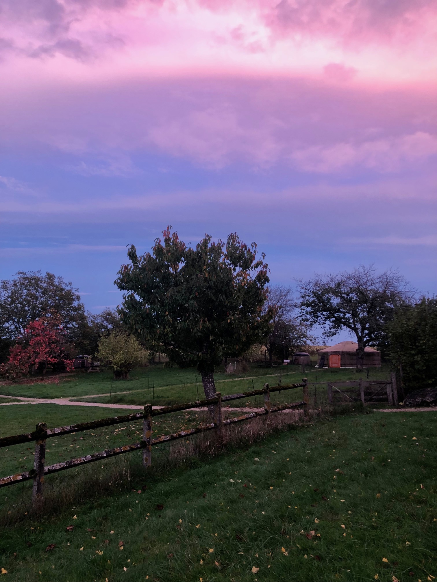 Gîte rural avec un jardin verdoyant et un ciel coloré au crépuscule.