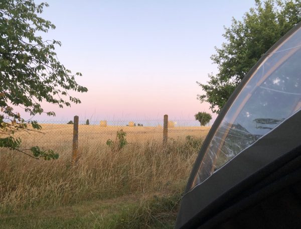Camping en tente avec vue sur des champs de foin au coucher du soleil.