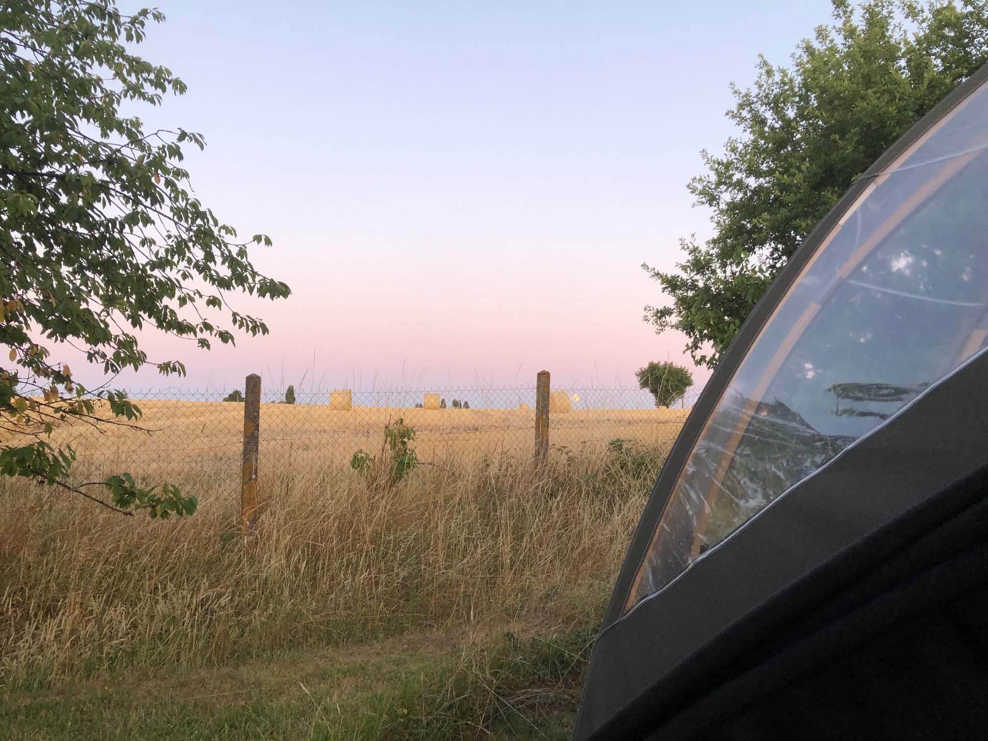 Camping en tente avec vue sur des champs de foin au coucher du soleil.