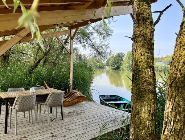 Cabane sur pilotis avec terrasse surplombant un paisible plan deau entouré de verdure.
