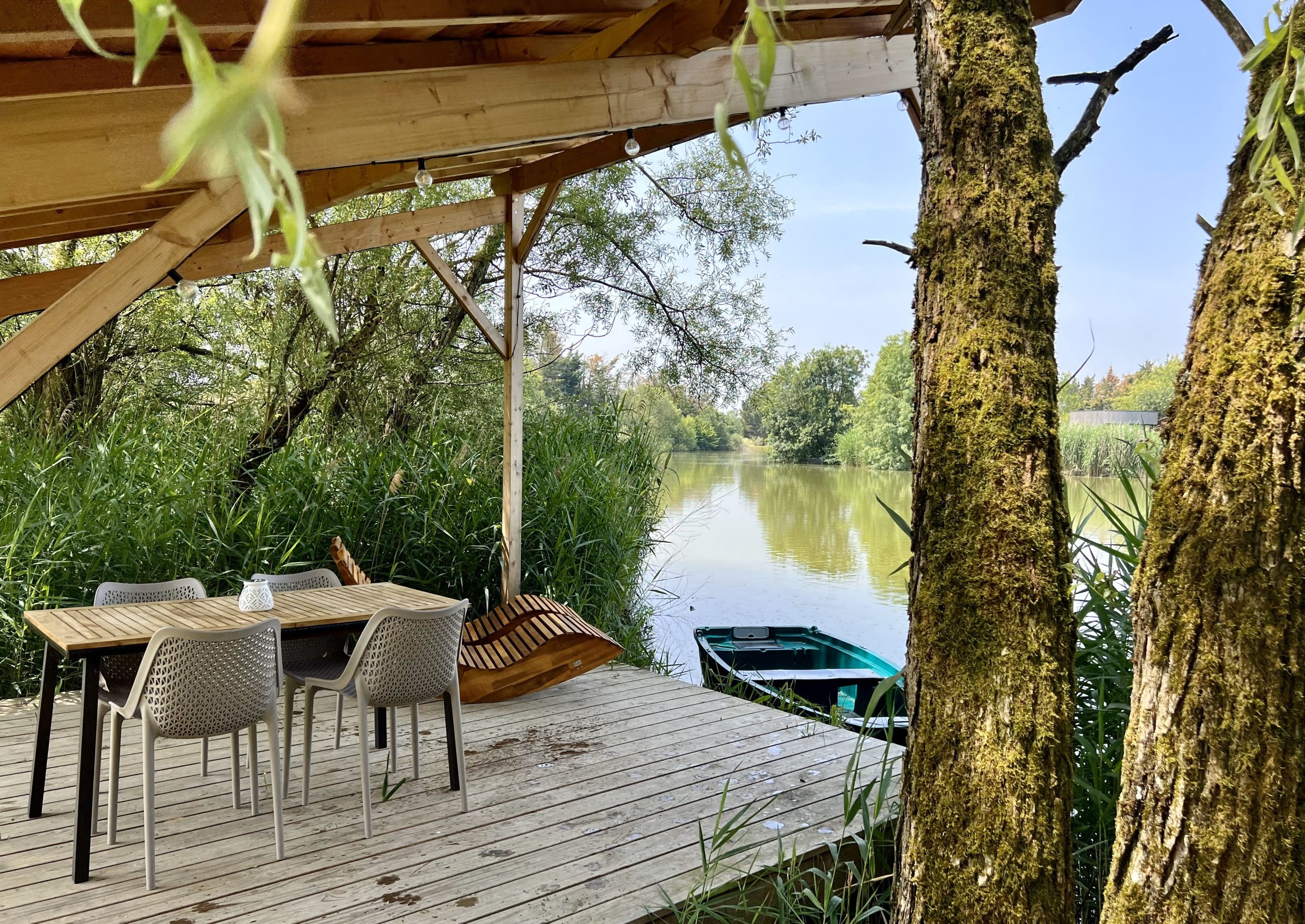 Cabane sur pilotis avec terrasse surplombant un paisible plan deau entouré de verdure.