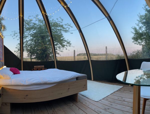 Cabane en verre avec lit douillet et vue sur la nature, décor coloré.