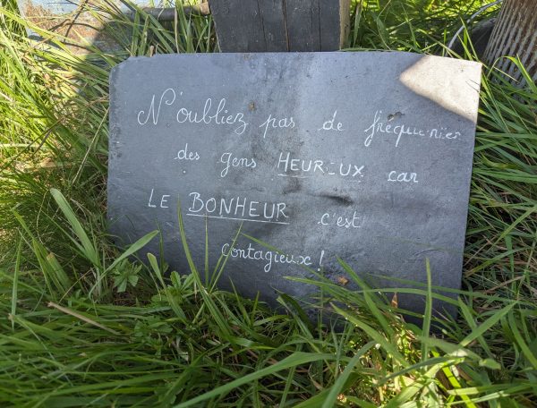 Gîte rural avec une jolie pancarte en ardoise sur lherbe verdoyante.