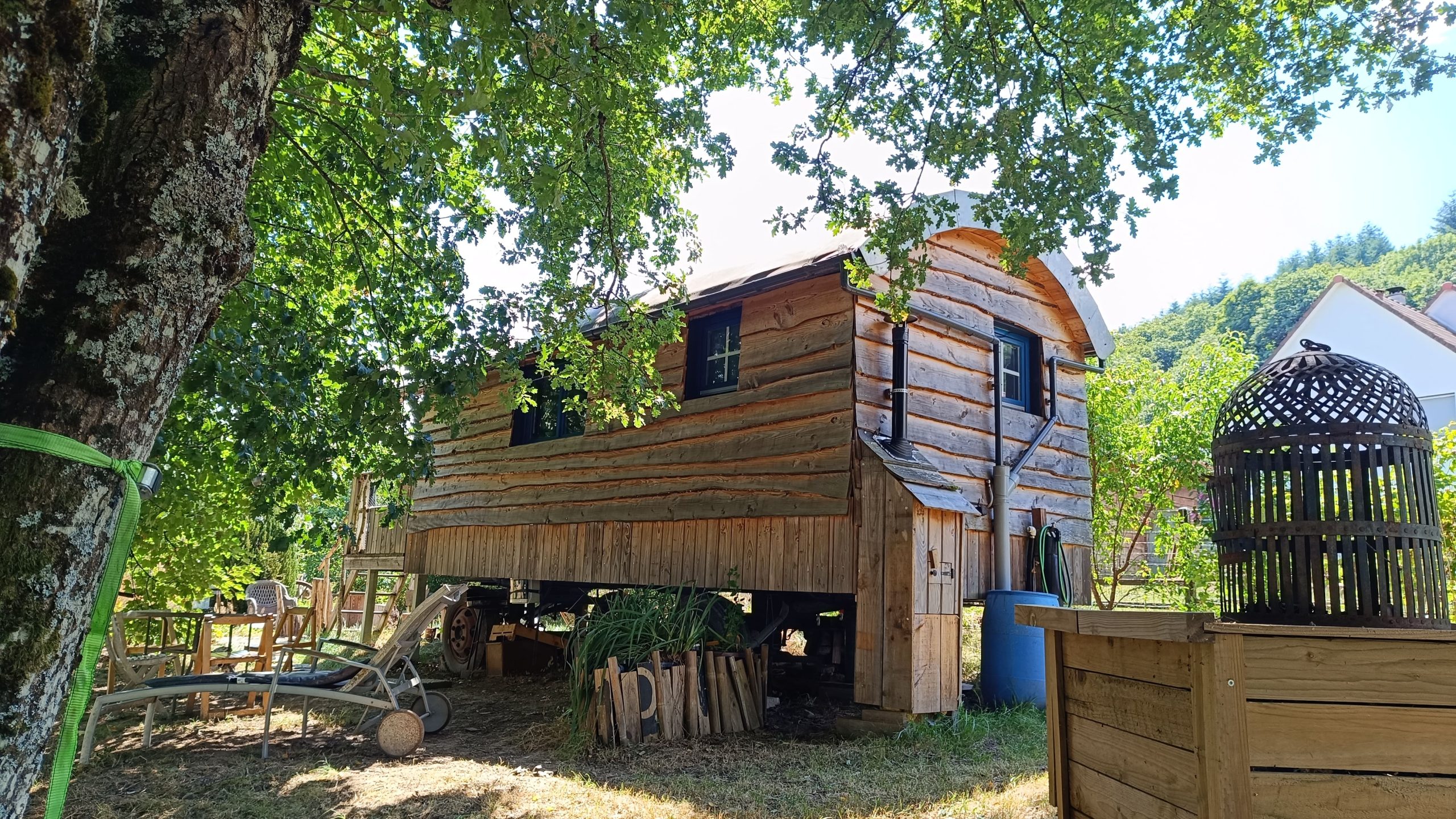Cabane en bois surélevée, entourée darbres verdoyants et dun jardin accueillant.