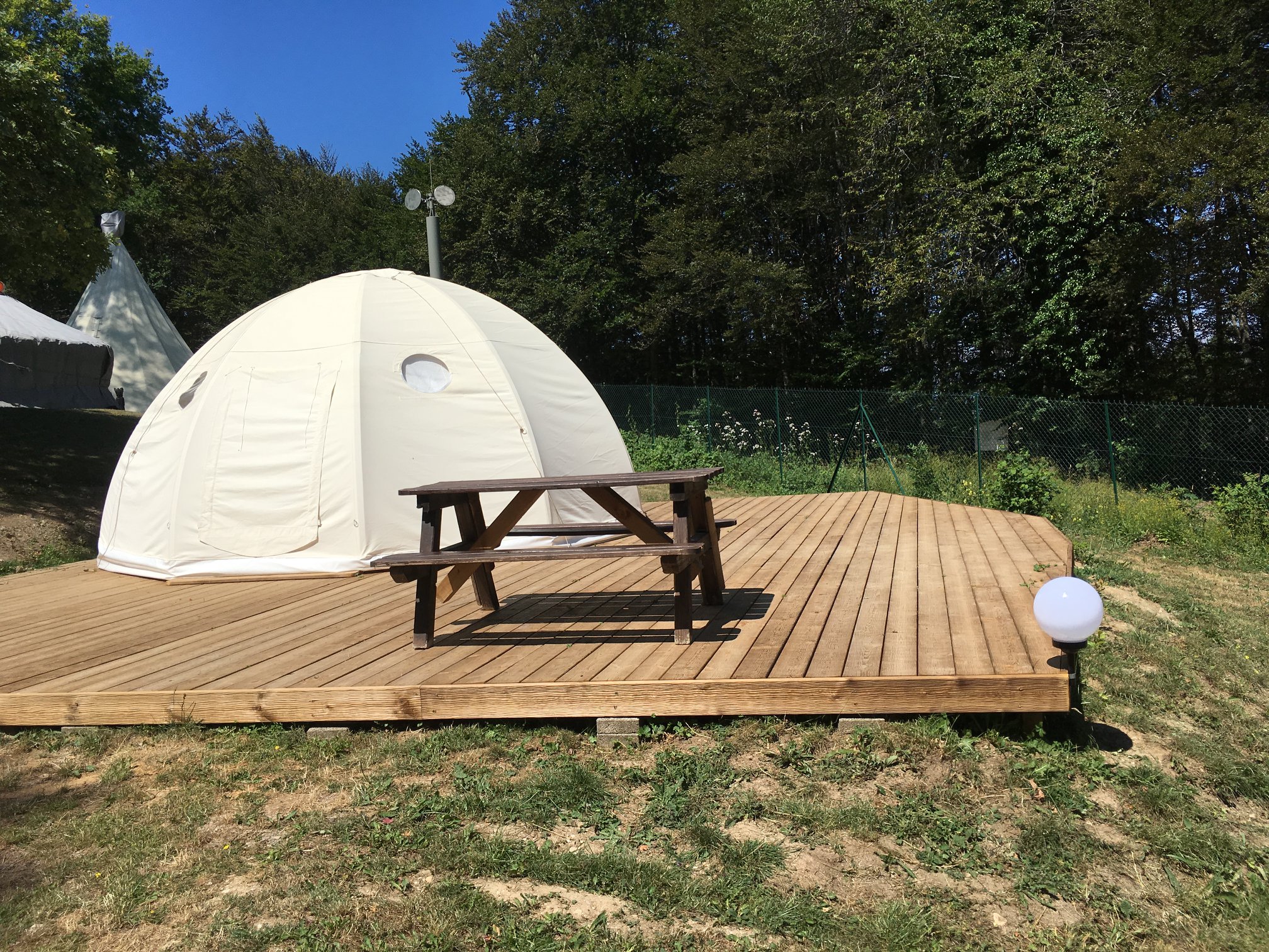 Dôme de glamping sur une terrasse en bois, entouré de verdure.