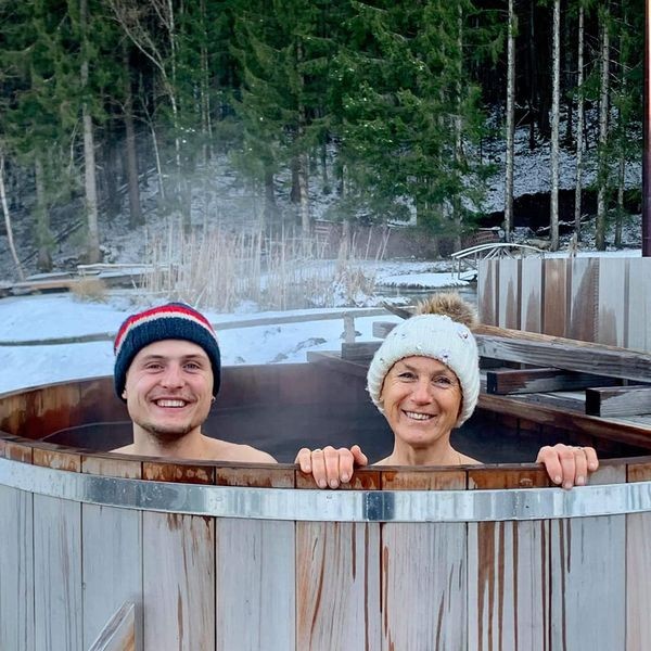 Bain nordique en bois, couple souriant dans un cadre naturel enneigé.