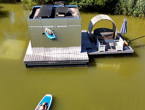 Cabane flottante moderne avec terrasse et kayak sur leau calme.