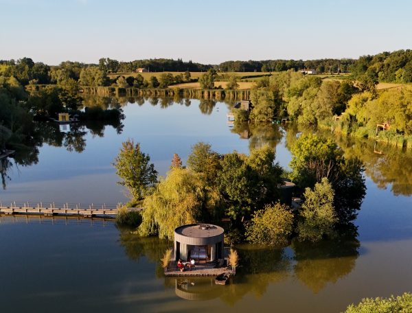 Cabane flottante sur un lac, entourée de verdure et deau calme.