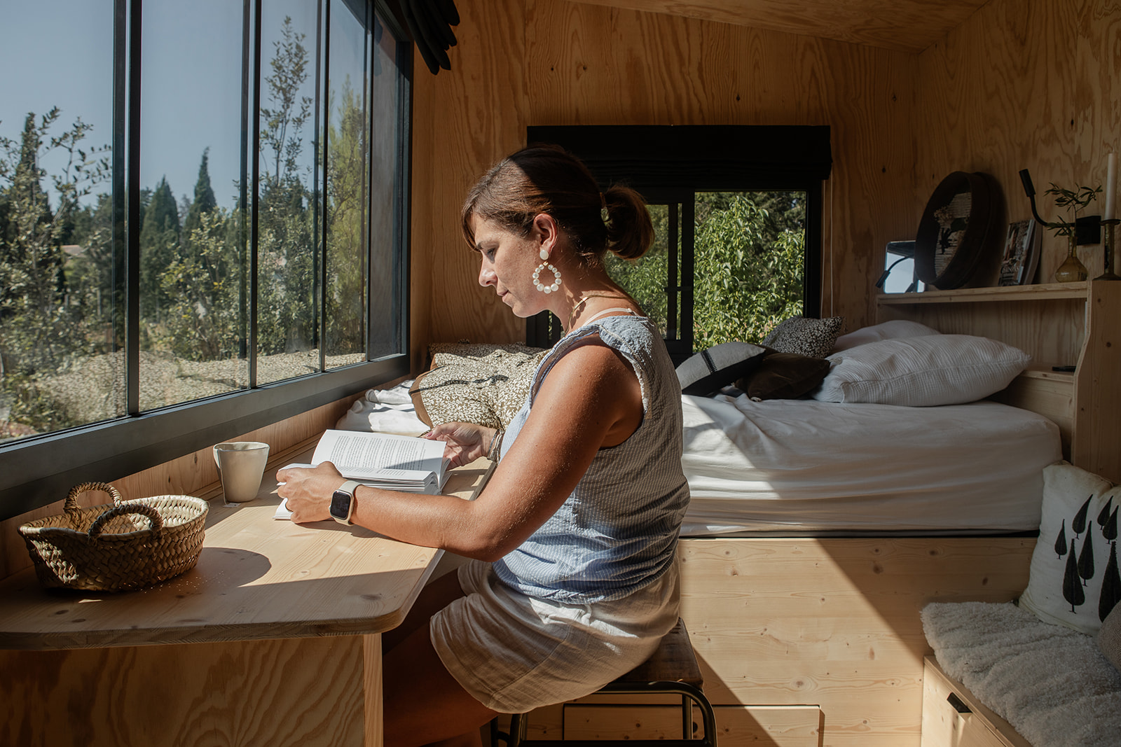 tiny-aout-139 Cabane en bois avec grandes fenêtres, offrant une vue sur la nature et un coin lecture cosy.