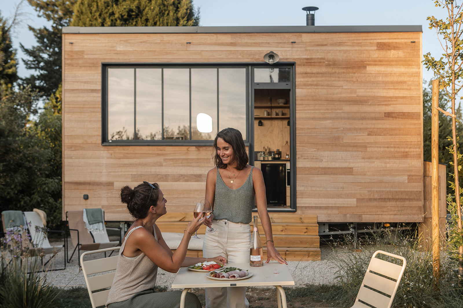 tiny-aout-77 Deux amies profitent d'un repas en extérieur devant une maison en bois moderne.